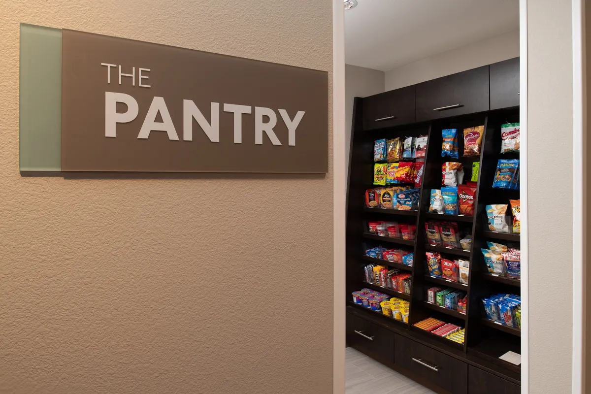 This image features 'THE PANTRY' sign above neatly organized shelves stocked with snacks, suggesting convenience for guests returning from local adventures. The scene is casual and inviting, highlighting opportunities for quick meals or impromptu gatherings after a day out exploring golf courses and wineries.