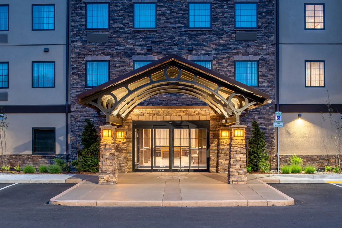 The image captures the hotel's main exterior, with a welcoming arched entryway, a sturdy stone facade, glowing lanterns, and large glass doors. The evening lighting creates an inviting ambiance, suggesting a safe and comfortable return after a day of exploration.