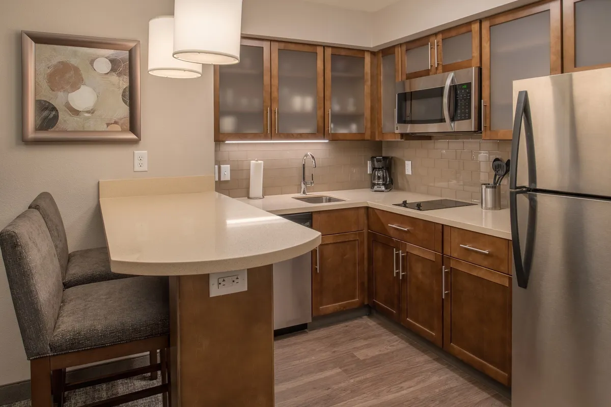 A contemporary kitchen space with a prominent kitchen island, shining stainless steel appliances, and tasteful wall art. The setting is bright and inviting, suggesting a space ideal for preparing meals, entertaining, or enjoying casual dining. The appliances visible include a stove, microwave, and fridge, and the kitchen island offers ample workspace for cooking or socializing.