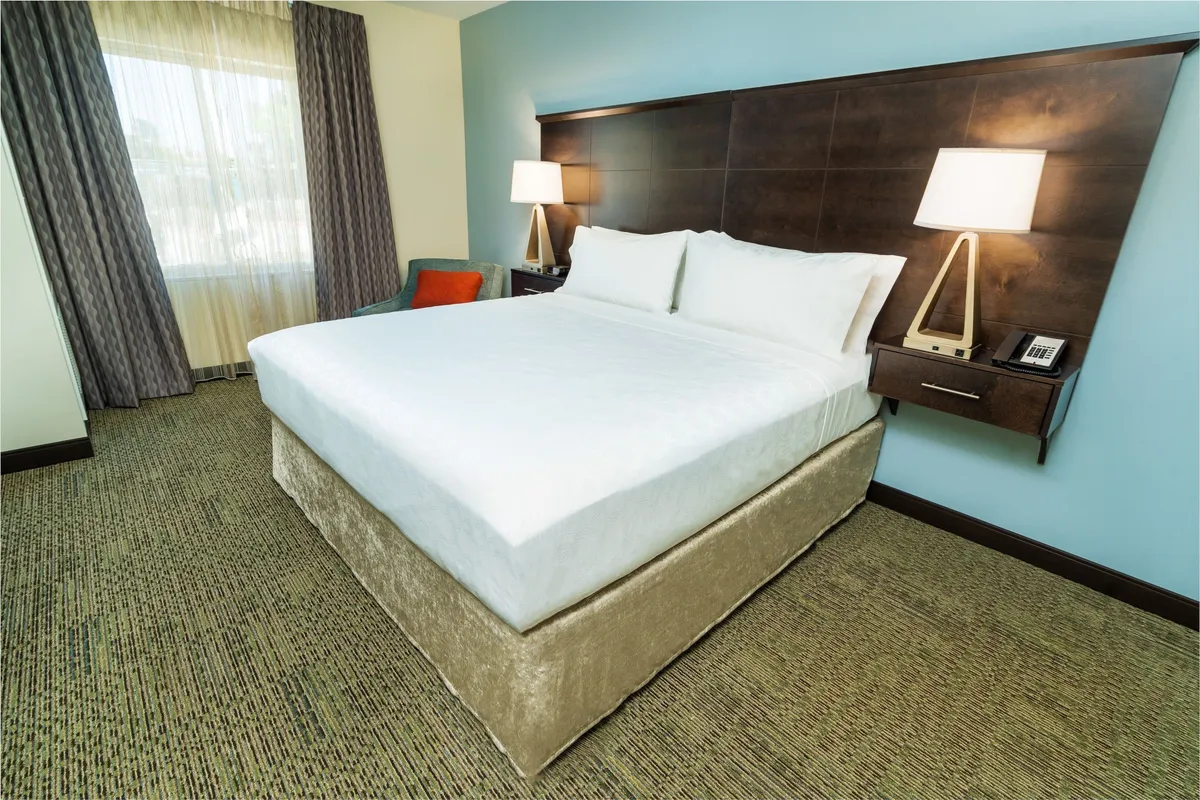 This image showcases a cozy bedroom featuring a plush King bed as the focal point, accompanied by a nightstand, lamp, and a window that allows in natural light. The layout emphasizes comfort and tranquility, with soft lighting and a serene ambiance that invites relaxation.