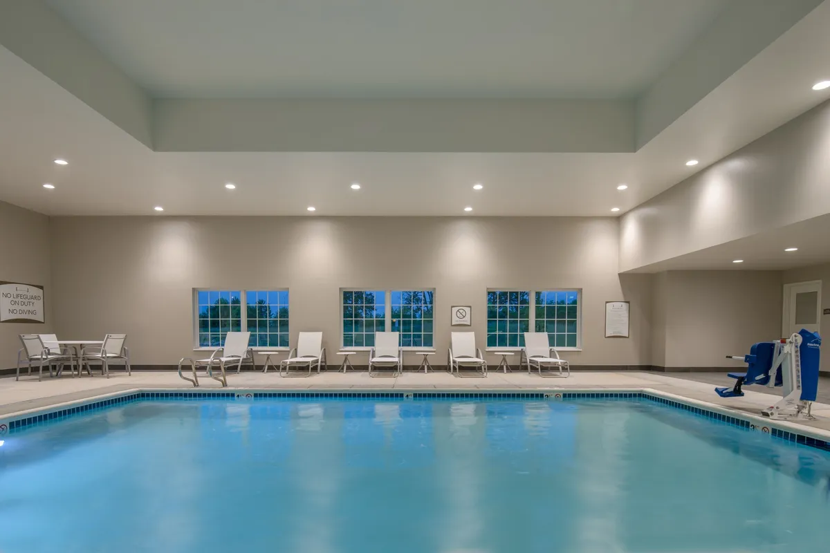 This image features a bright, inviting heated indoor swimming pool surrounded by comfortable lounge chairs, large windows letting in natural light, and functional poolside equipment. The relaxed and rejuvenating mood is ideal for guests seeking leisure and family-friendly fun.